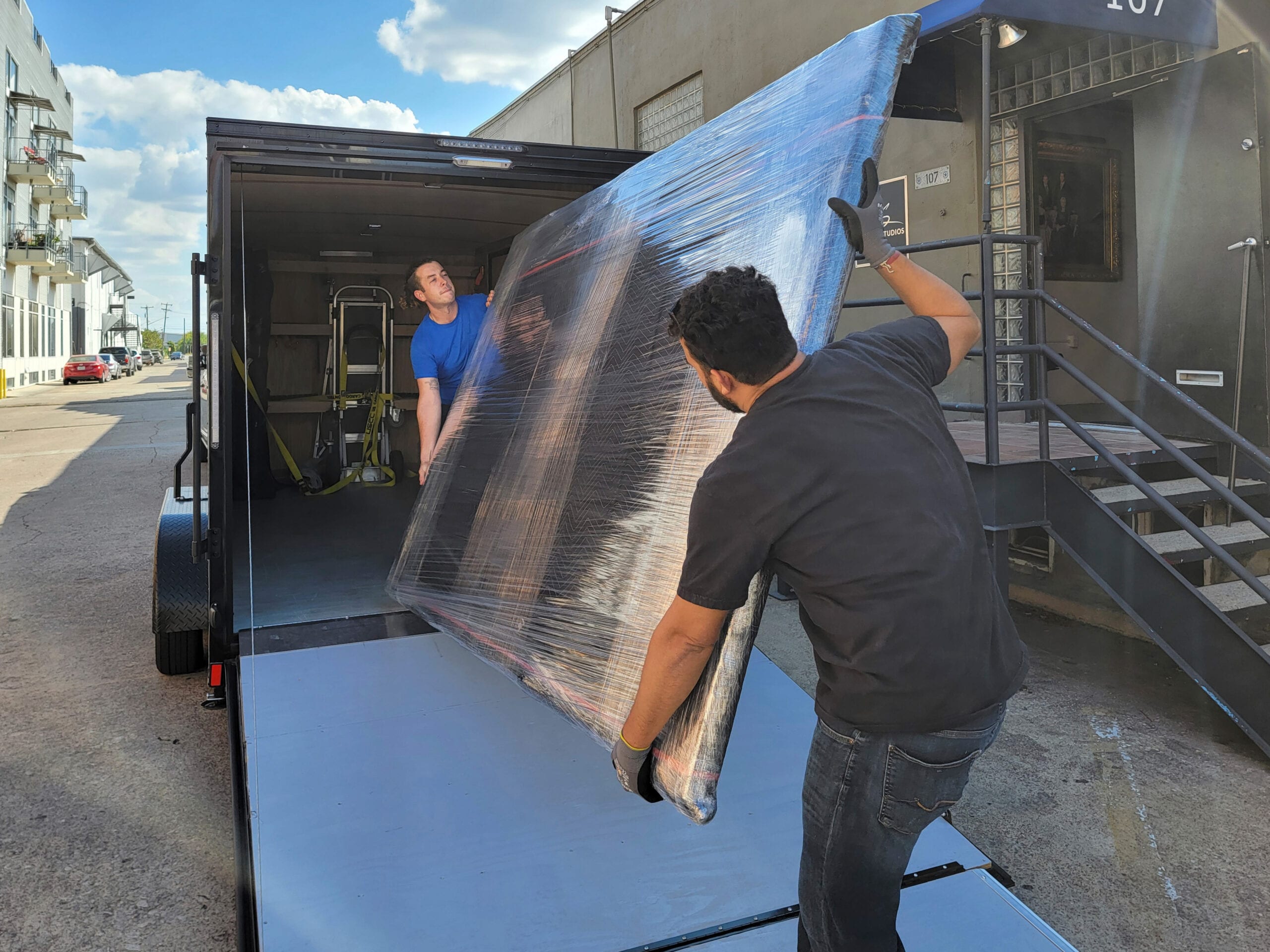 Two KGS Studios team members carefully loading a large, wrapped fine art piece onto a ramp into a custom art transport trailer, demonstrating white-glove delivery expertise.