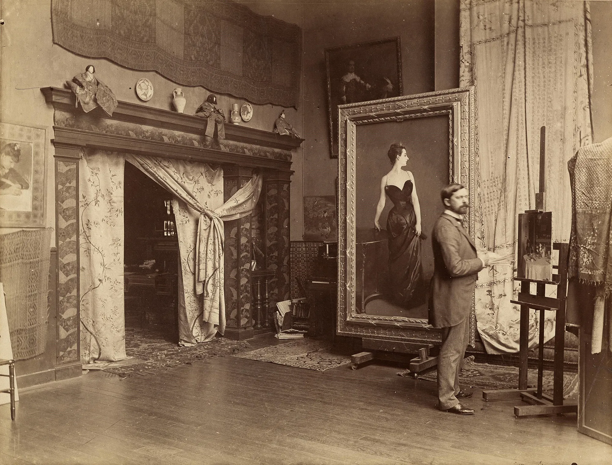 A historical photograph of master artist John Singer Sargent in his Paris studio, standing beside his iconic masterpiece portrait,